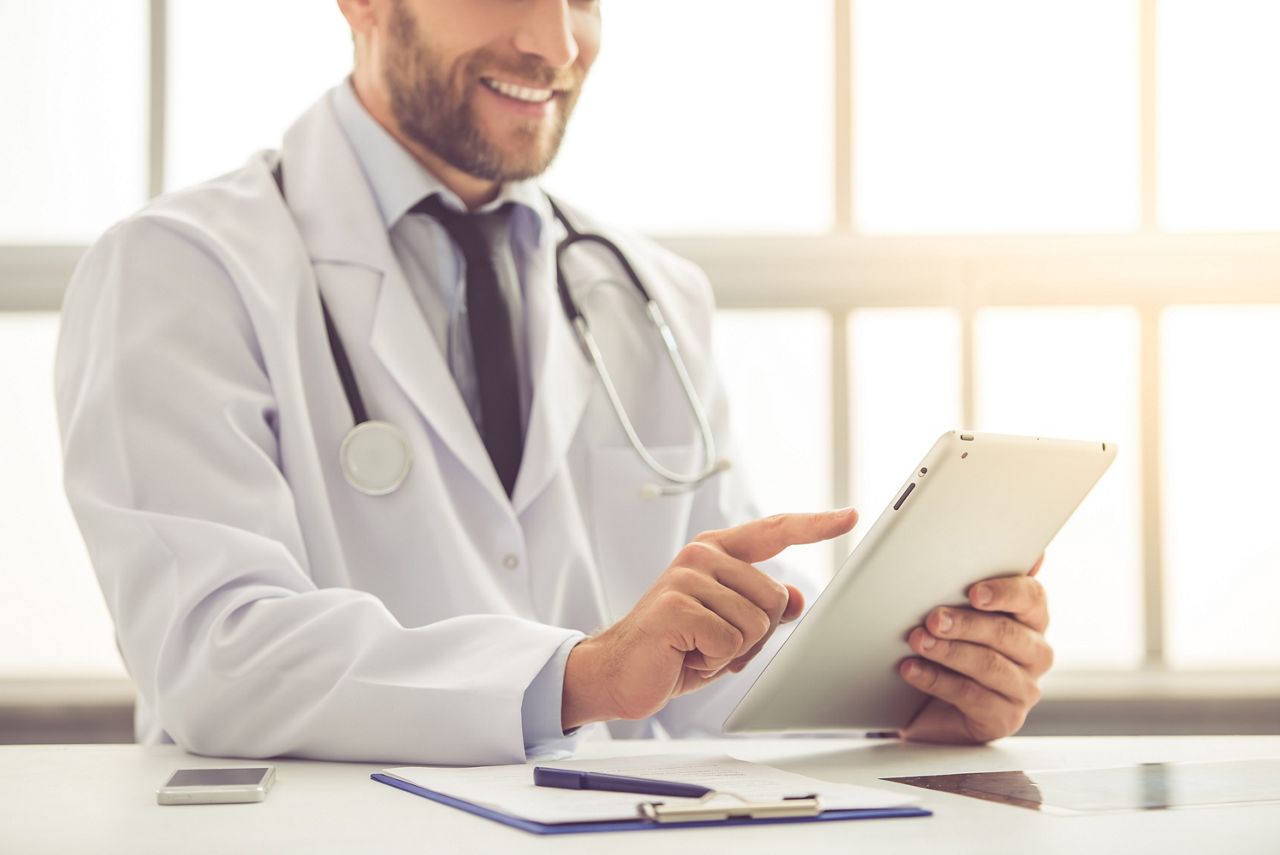 Cropped image of handsome medical doctor in white coat using a digital tablet and smiling while working in his office