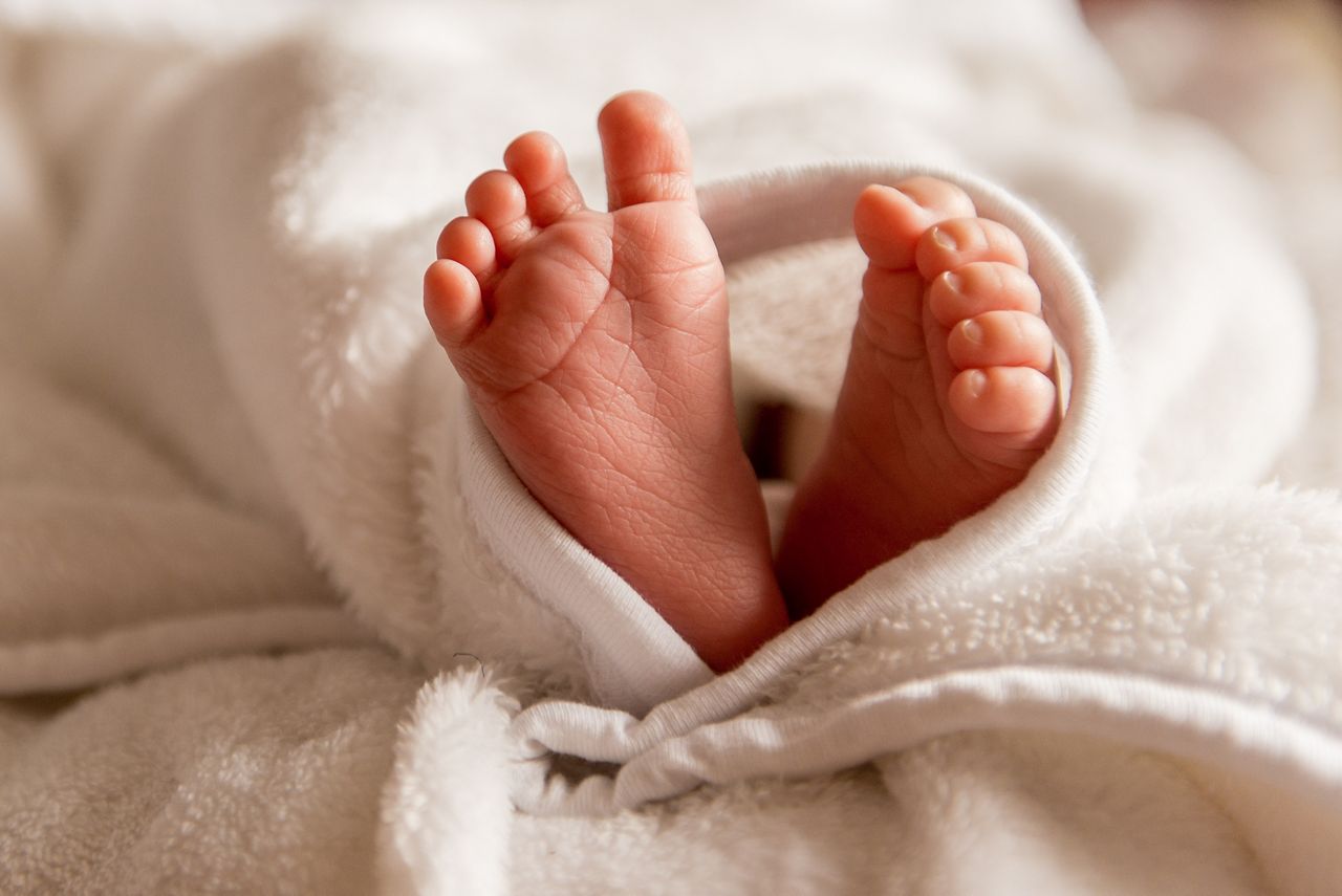 Bare feet of a cute newborn baby in warm white blanket. Childhood. Small bare feet of a little baby girl or boy. Sleeping newborn child.