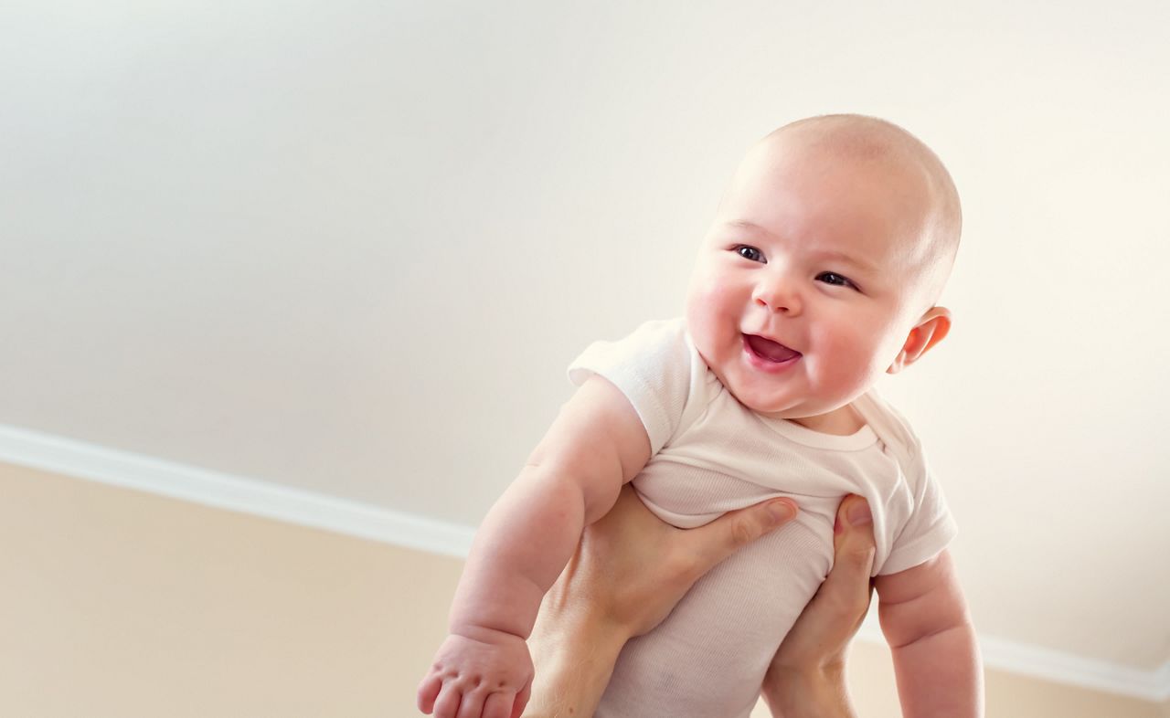 Happy infant baby girl being held up in the air by her parent
