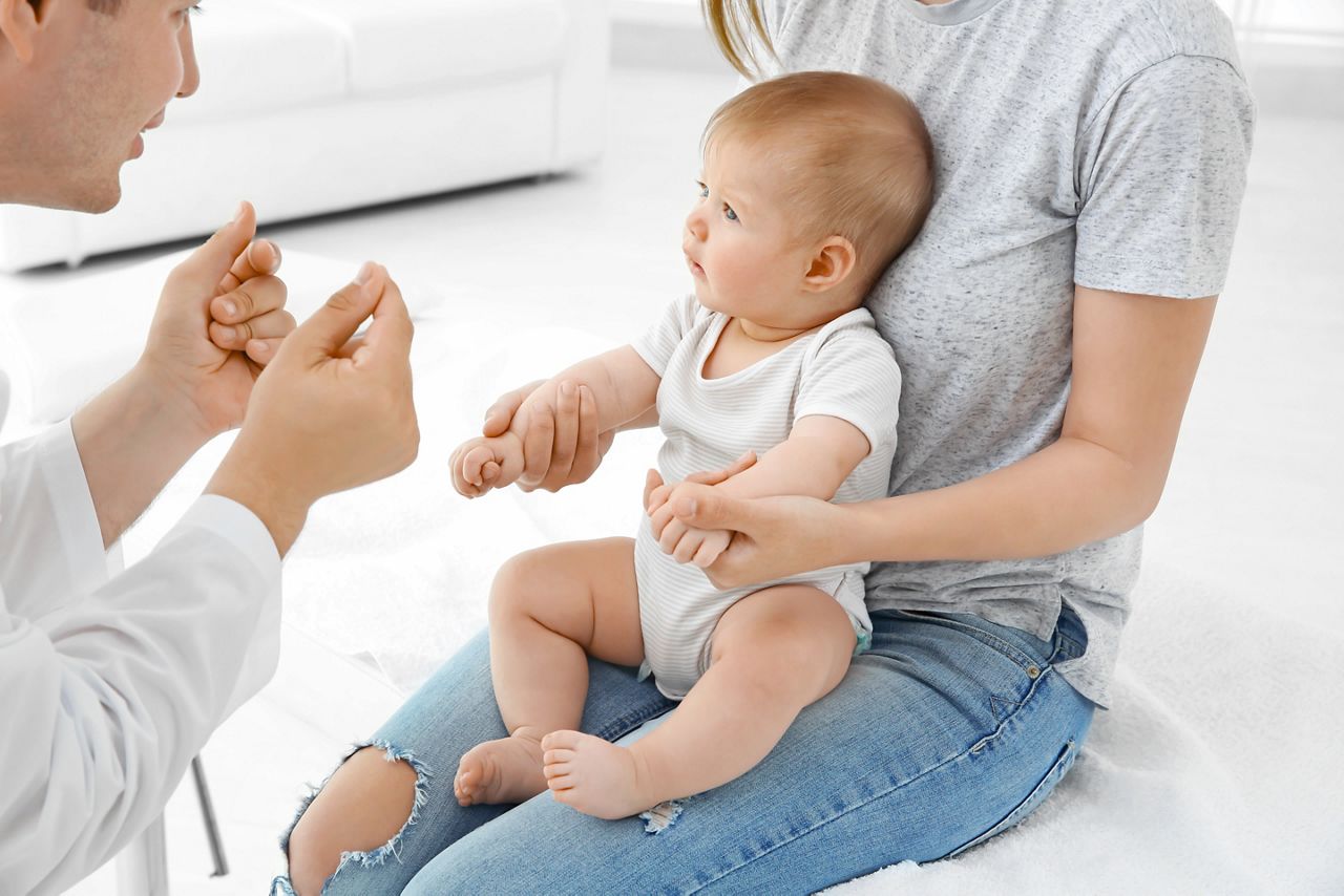 Young mom holding her cute baby while doctor working