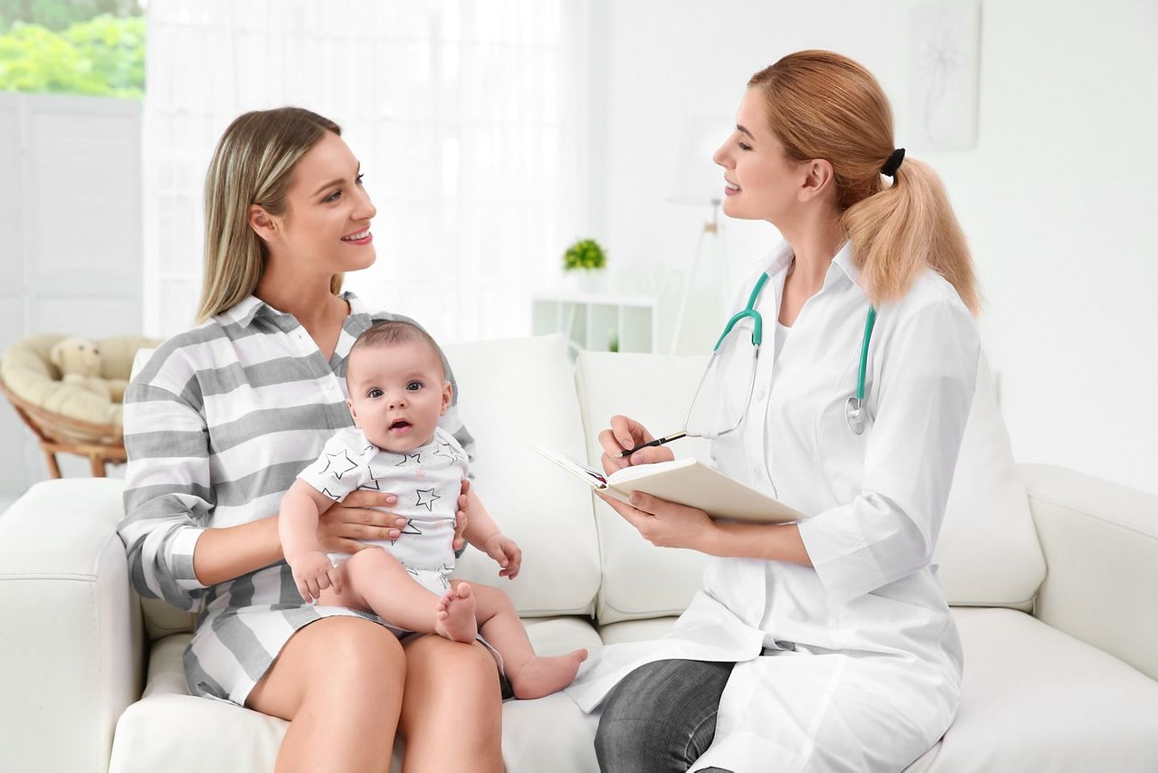 Doctor writing something in notebook and mother with baby at home