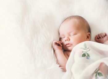 Sleeping newborn baby in a wrap on white blanket. Beautiful portrait of little child girl 7 days, one week old.