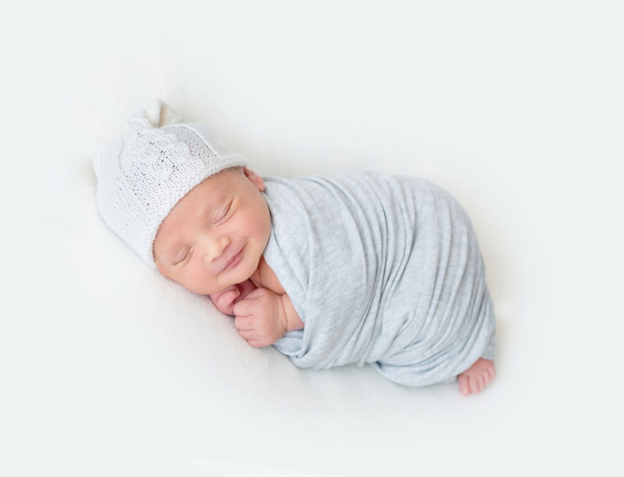 Newborn baby boy swaddled in a light blue wrap sleeping on a soft white surface.