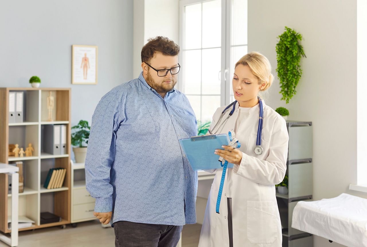 Patient and doctor consultation in medical clinic. Overweight fat man listens as female physician reviews notes, discusses obesity risks and treatment. Healthcare guidance and support concept.