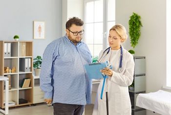 Patient and doctor consultation in medical clinic. Overweight fat man listens as female physician reviews notes, discusses obesity risks and treatment. Healthcare guidance and support concept.