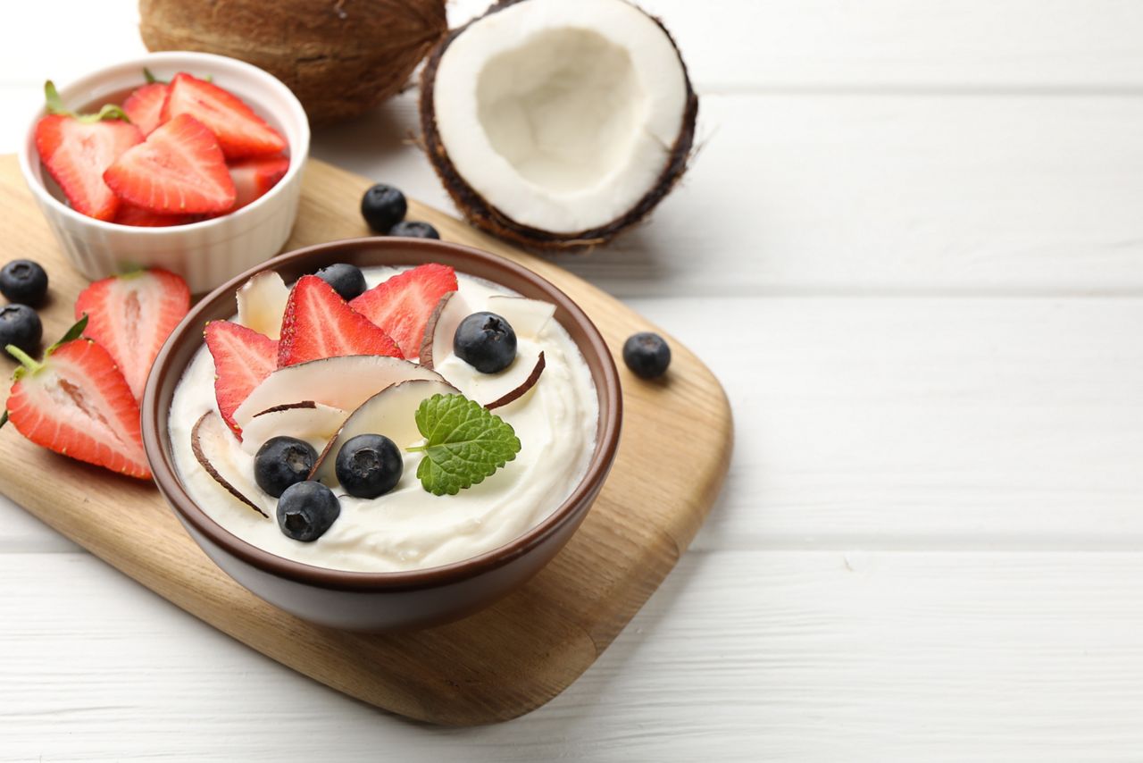 Tasty yogurt with coconut and berries served on white wooden table, closeup. Space for text