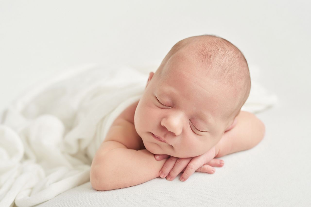 Cute newborn baby lies swaddled in a white blanket. Baby goods packaging template. Closeup portrait of newborn baby with smile on face. Healthy and medical concept. 