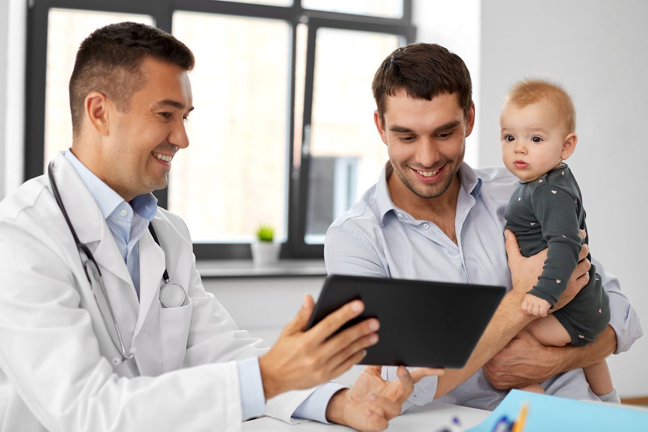 medicine, healthcare, pediatry and people concept - happy doctor showing tablet computer to father with baby daughter at medical office in hospital