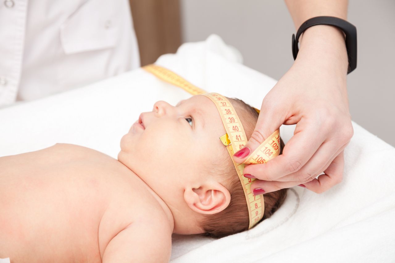 Close-up shot of pediatrician examines two months baby boy. Doctor using measurement tape checking baby head size