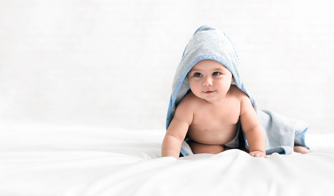 Bedding time. Adorable baby wearing hooded towel after bath crawling on bed, copy space