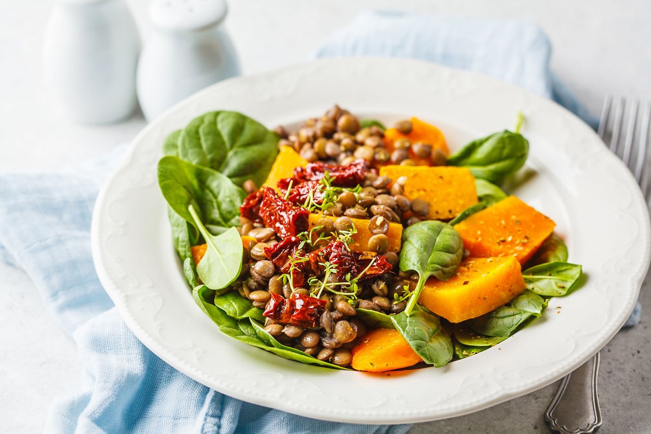 Vegan salad with lentils, pumpkin and dried tomatoes in a white plate.