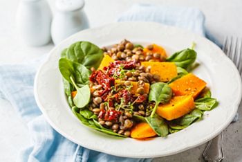 Vegan salad with lentils, pumpkin and dried tomatoes in a white plate.
