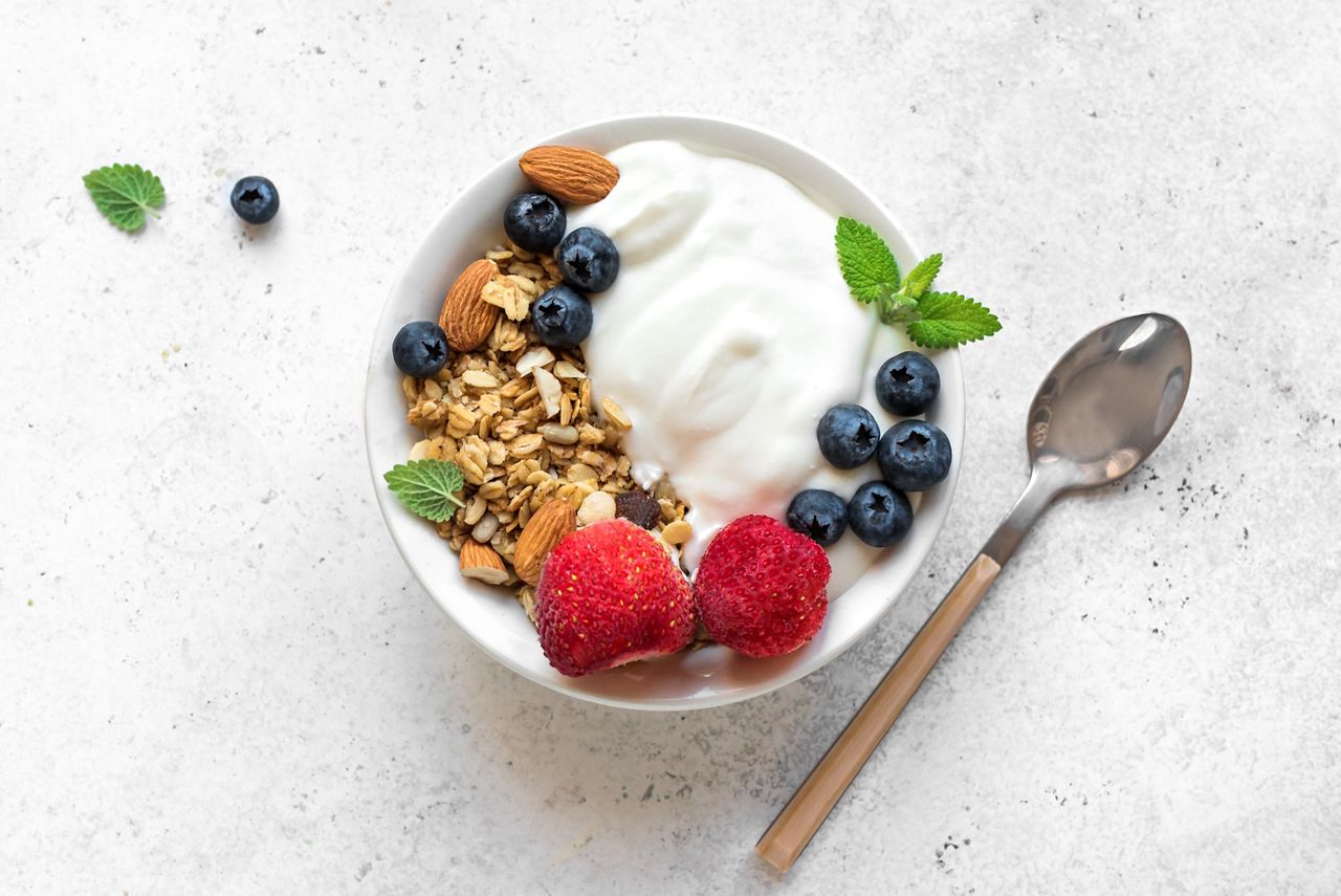 Granola with yogurt and berries for healthy breakfast. Bowl of greek yogurt with granola, almonds, blueberries and strawberries, top view, copy space.