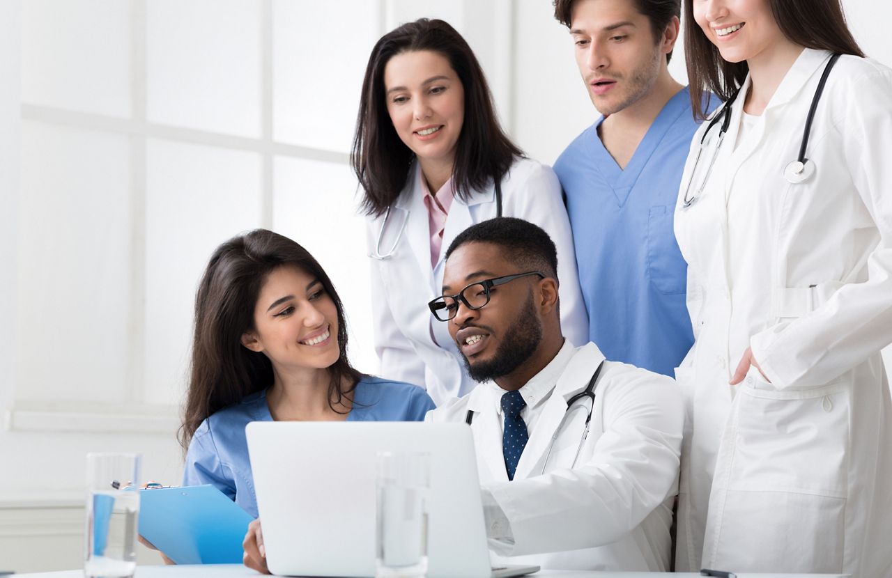 Team of interns and practitioners examining medical reports at hospital, using laptop