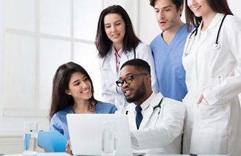 Team of interns and practitioners examining medical reports at hospital, using laptop