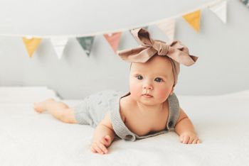 Portrait of a cute 3 months baby lying down on a blanket, bow on the head.