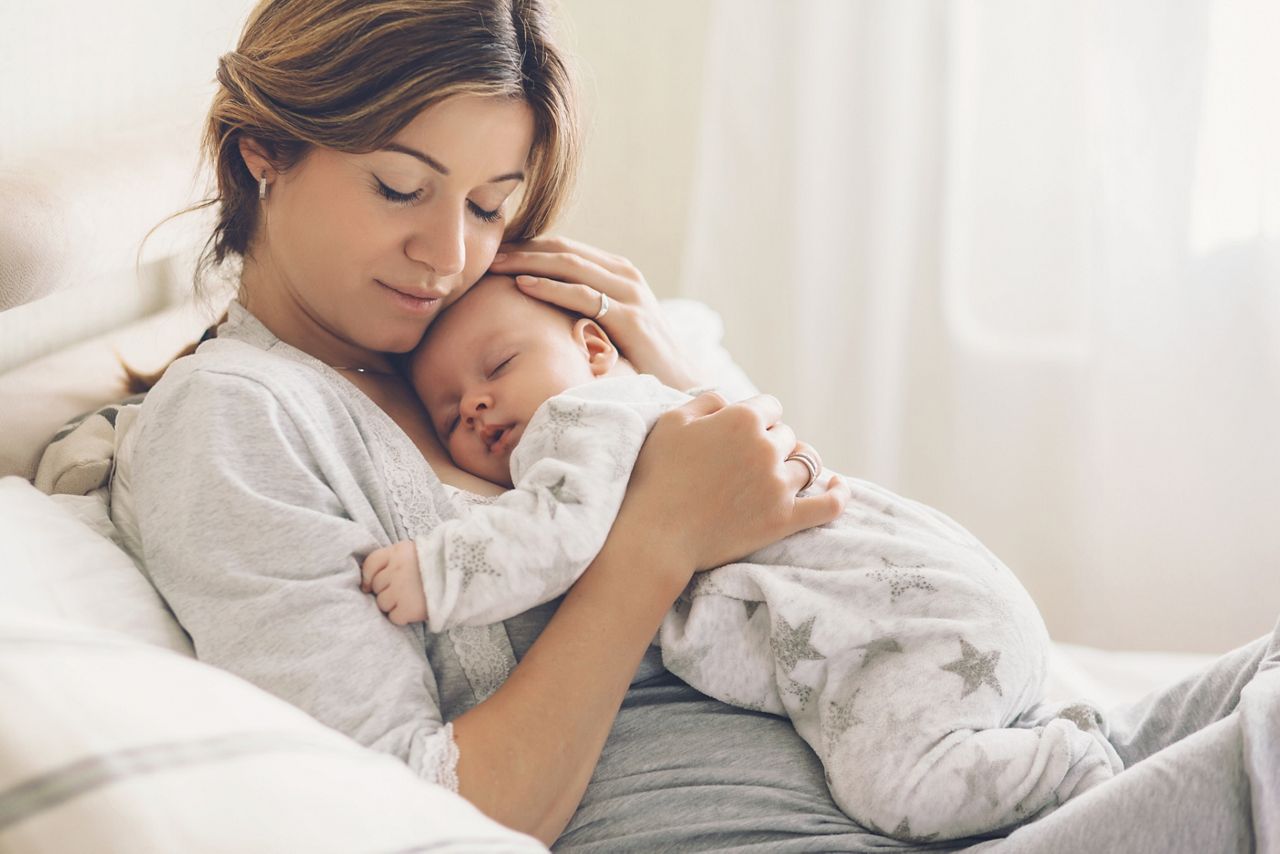 Loving mom carying of her newborn baby at home. Bright portrait of happy mum holding sleeping infant child on hands. Mother hugging her little 2 months old son.