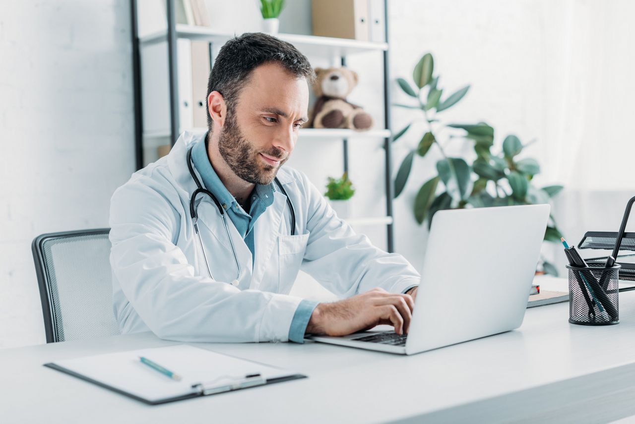 positive doctor sitting at workplace and using laptop