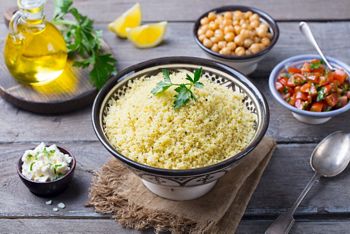 Couscous in bowl with olive oil. Wooden background. Close up.