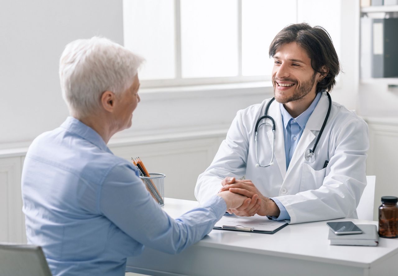 Medical empathy concept. Caring doctor holding hand of senior woman at visit