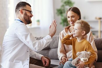 family doctor pediatrician conducts examination of child boy who came with his mother,  and giving high five to him  
