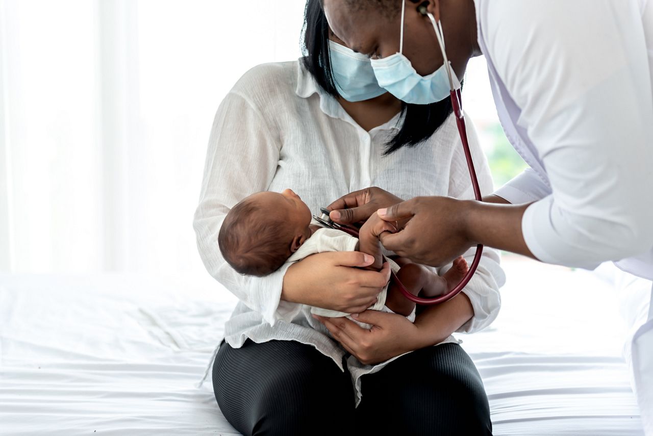 African doctor wearing surgical mans and using a stethoscope, checking the respiratory system and heartbeat Of a 12-day-old baby newborn, who is half African half Thai, to Infant health care and treatment concept.