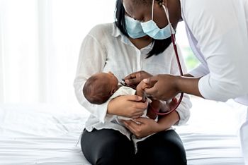 African doctor wearing surgical mans and using a stethoscope, checking the respiratory system and heartbeat Of a 12-day-old baby newborn, who is half African half Thai, to Infant health care and treatment concept.