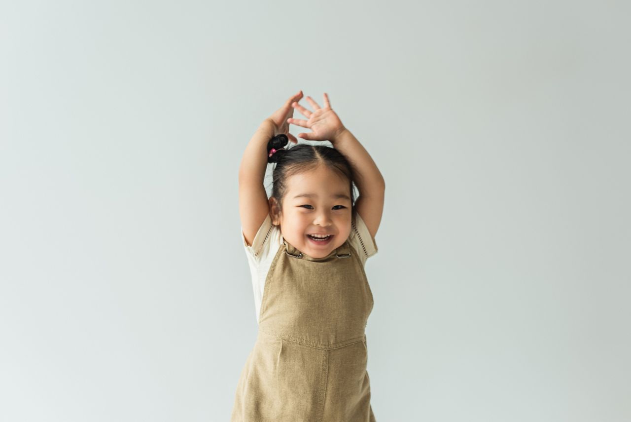 happy asian toddler girl with raised hands isolated on grey