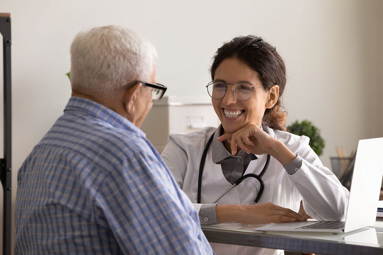 Happy friendly GP doctor meeting with senior 80s male patient, talking to old man, laughing at joke. Young therapist giving consultation, medical treatment advice at appointment. Elderly healthcare