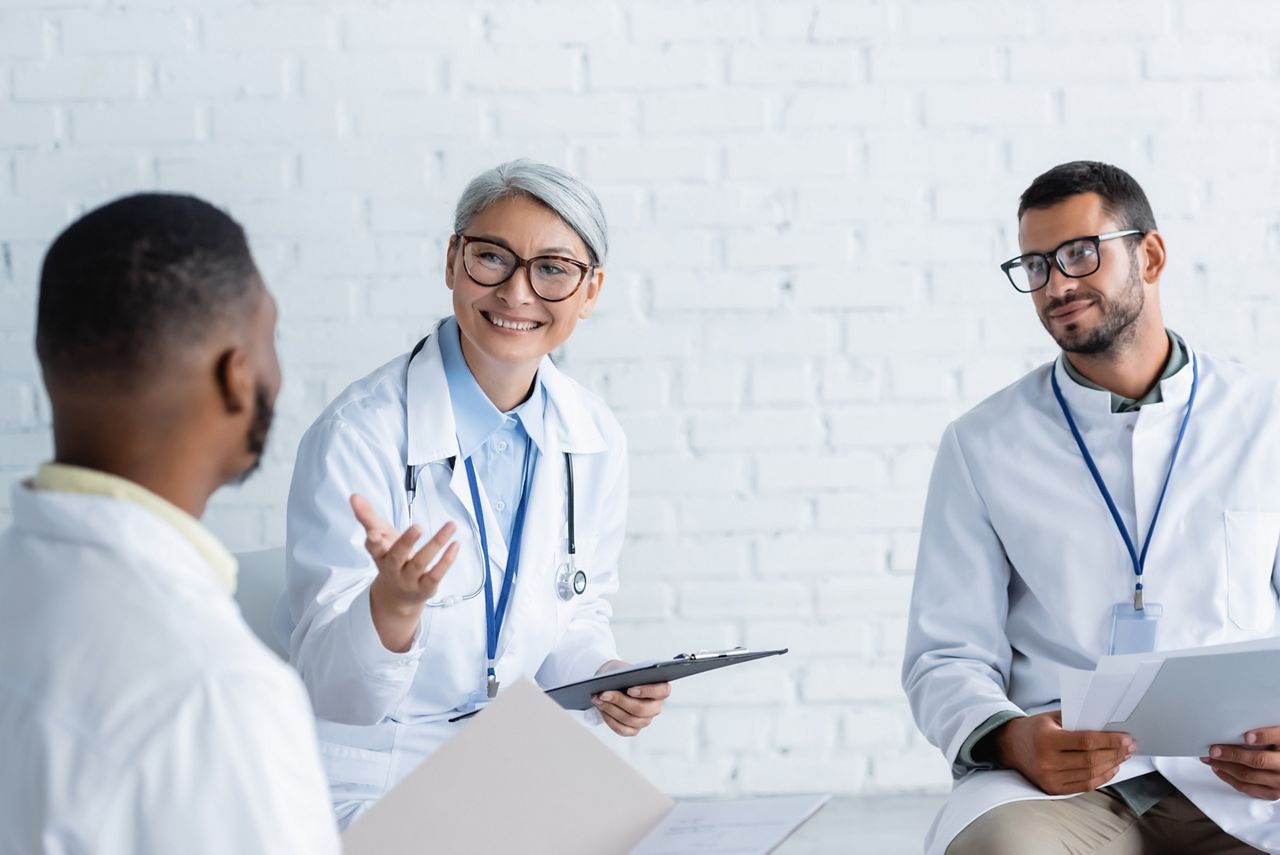 smiling asian doctor pointing at blurred african colleague during discussion