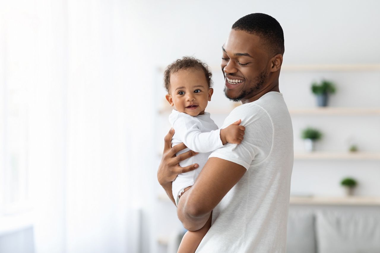 Happiness Of Fatherhood. Portrait of young black dad with cute little baby on his hands standing near window at home, loving african american father spending time with infant child, copy space