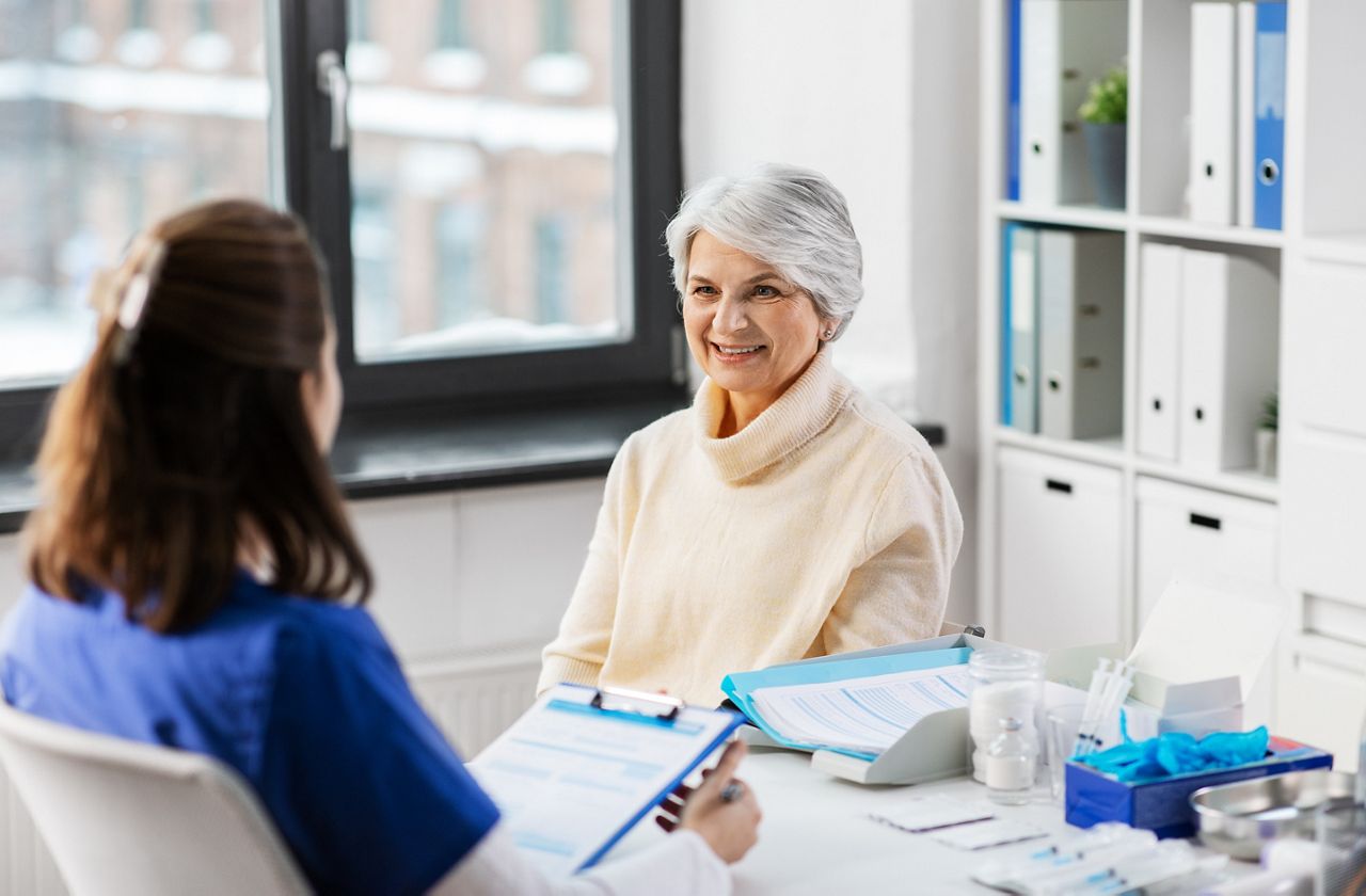 medicine, health and vaccination concept - doctor with clipboard and senior woman at hospital