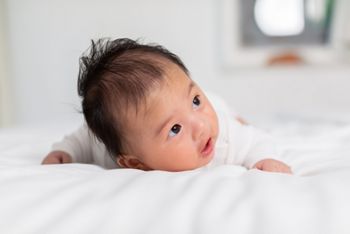 Newborn baby 3 month laying on stomach developing neck control .tummy time for strengthen baby neck and shoulder muscles.Cute infant lying crawling on white bed happiness and fun.Tummy Time Concept