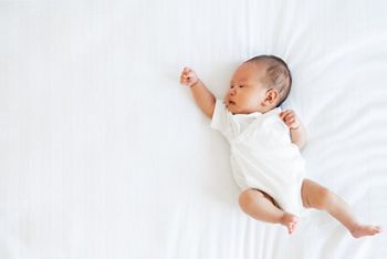 Portrait of Asian newborn baby in white cloth on bed funny pos