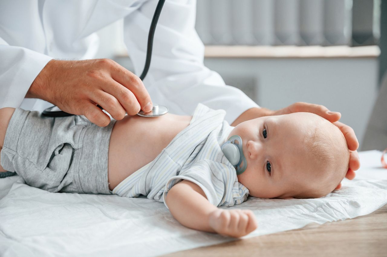 Close up view. Using stethoscope. Doctor in white coat is taking care of little toddler indoors.
