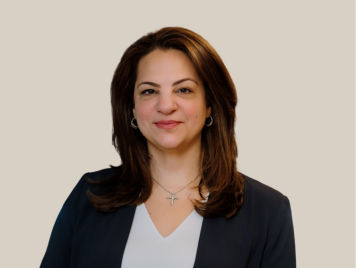 Angie Balian, Senior Vice President of Marketing and E-commerce at Danone Canada, smiles brightly, wearing a black blazer and a black shirt. He has short straight hair, styled with a topknot.