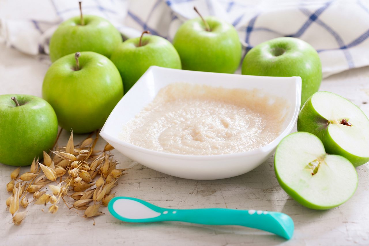 Baby food. Bowl of oatmeal porridge with fresh apples on wooden table