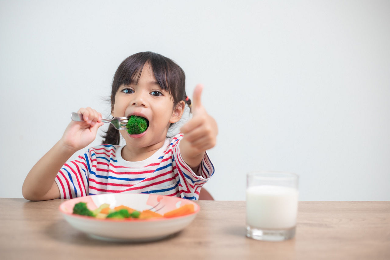 Cute asian child girl eating healthy vegetables and milk for her meal