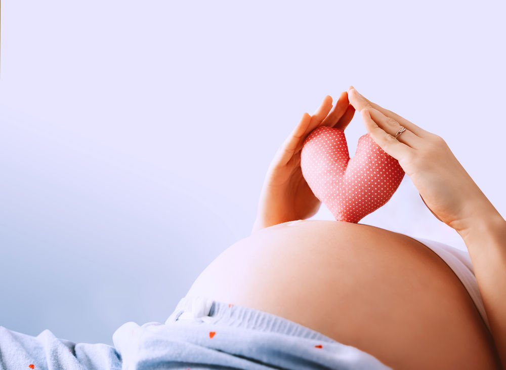 Pregnant woman holds in palms symbol in heart shape. Loving mom waiting of a baby. Concept of maternity, parenting, prepare and expect. Happy expectant mother during pregnancy.