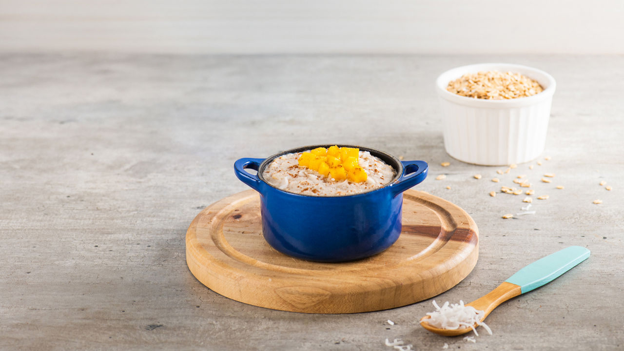Un tazón de avena cremosa con coco rallado, canela y trozos de mango, servido como una comida nutritiva para niños pequeños