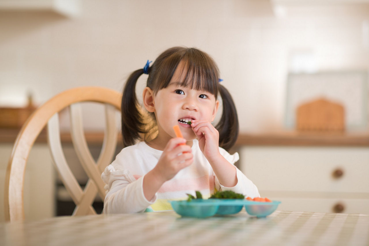 young girl eating fresh green vegetables against real kitchen background