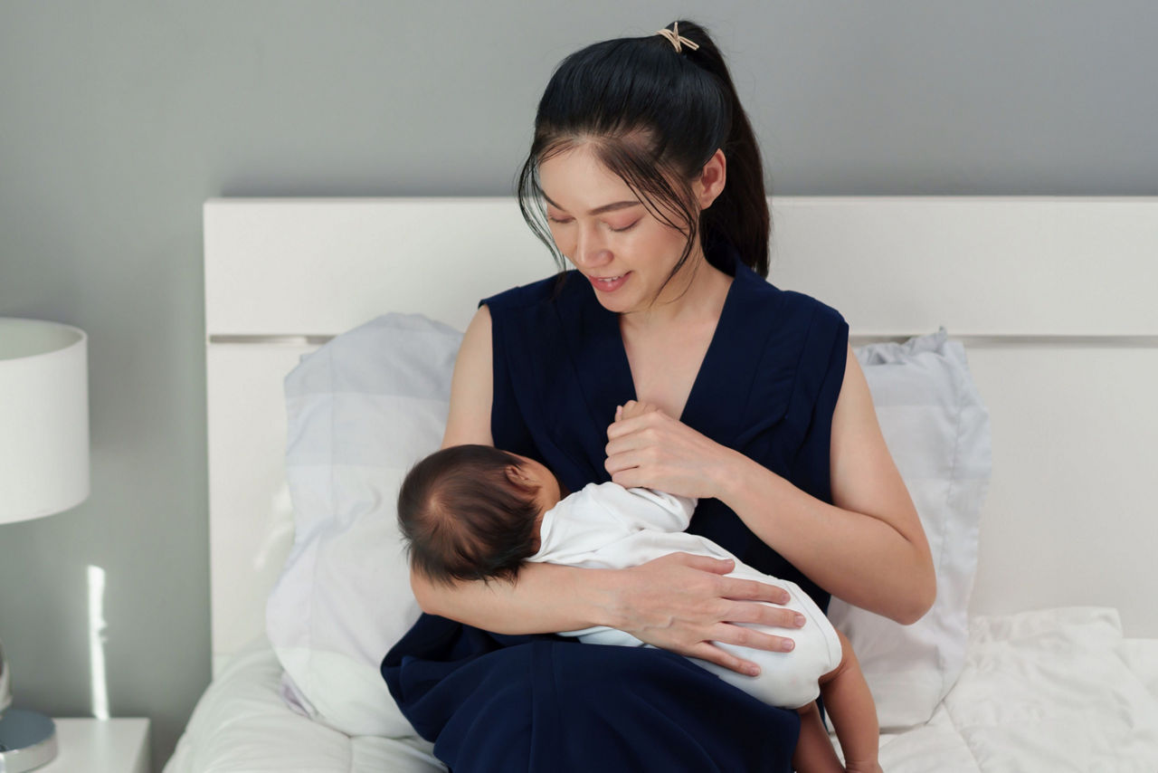 mother breastfeeding newborm baby on a bed
