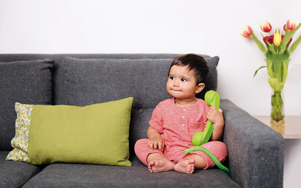 Baby sitting on a couch with a green phone in its hand