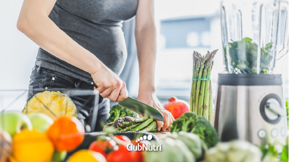 Mujer embarazada cocinando alimentos nutritivos.