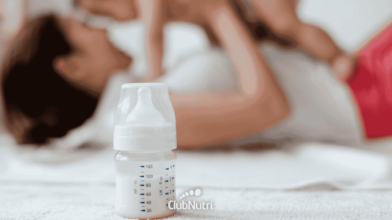 Mamadera en primer plano con una mamá con su bebé de fondo
