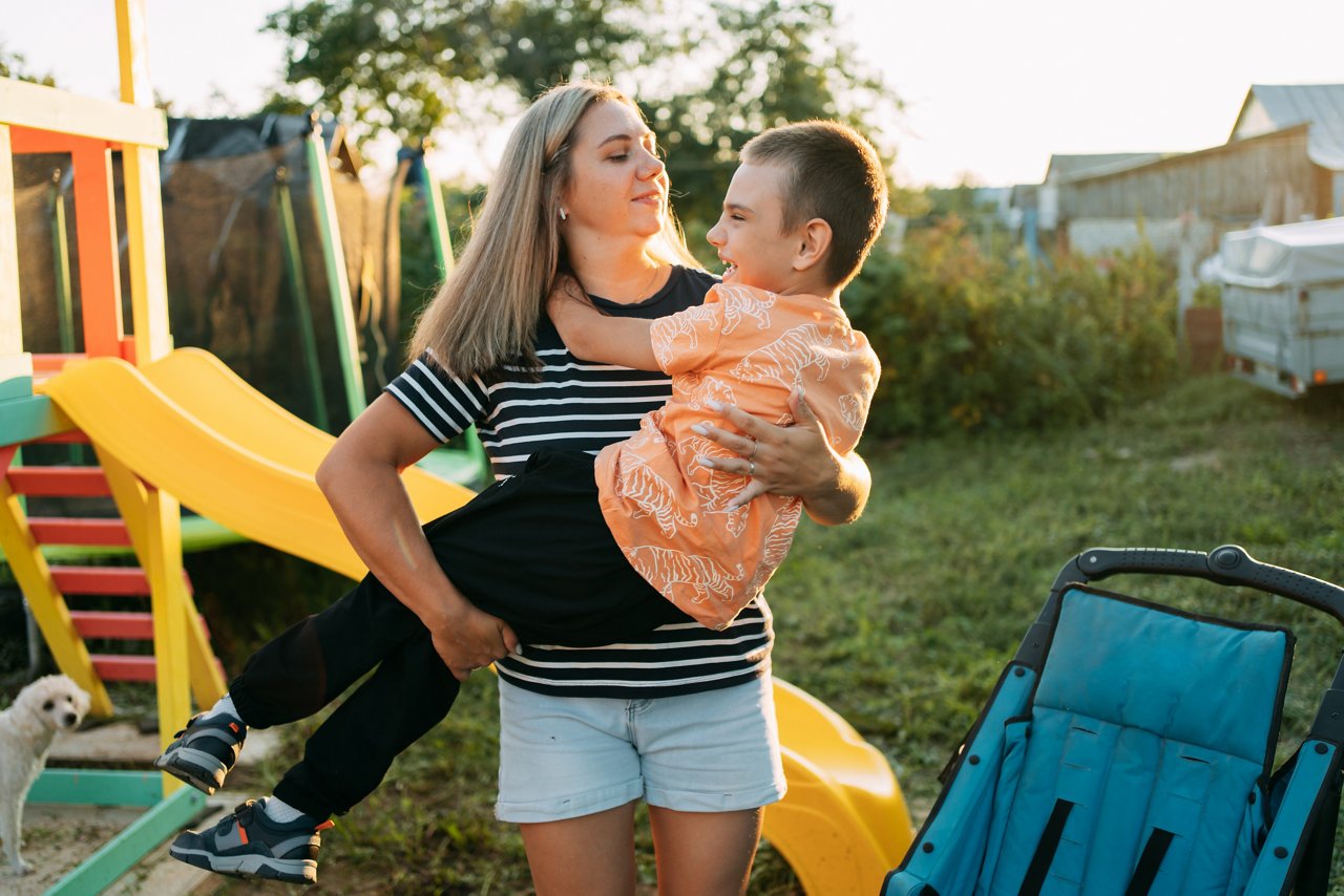mother hugs her son with cerebral palsy on a walk on a summer evening