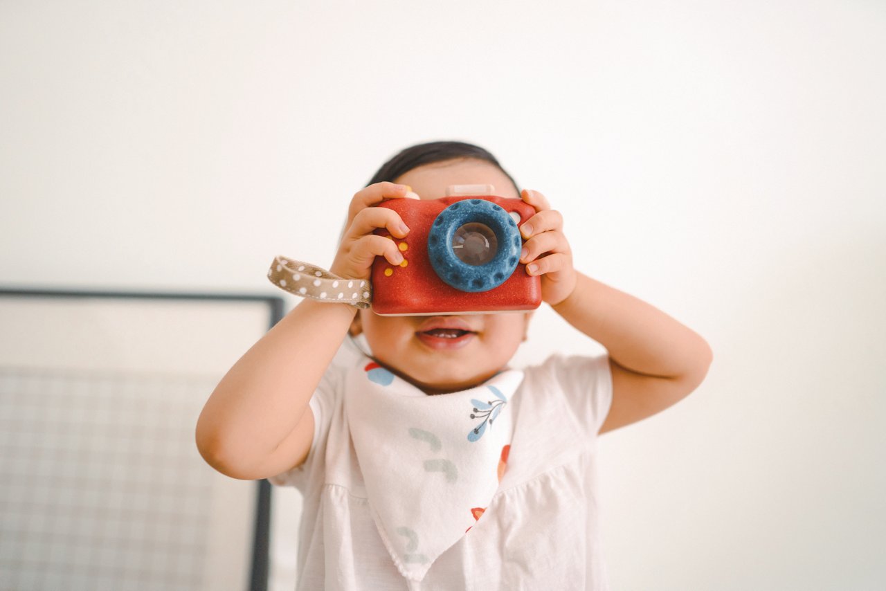 Cute little toddler girl having fun and taking photos with toy camera at home