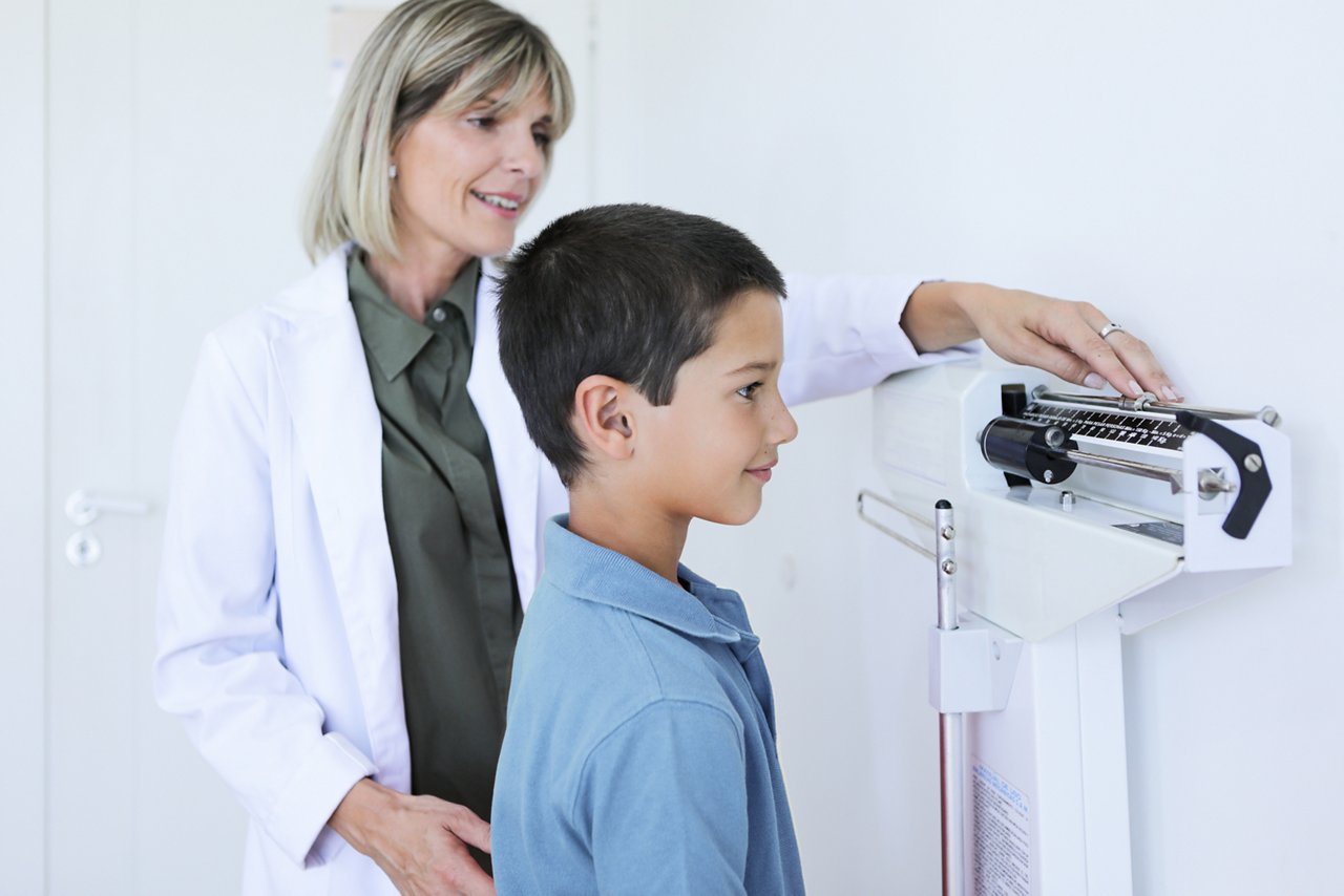 Argentinean nutritionist woman mesuring height and weight of a 8 years-old boy at proffesional balance in the medical office during a medical control - Buenos Aires - Argentina