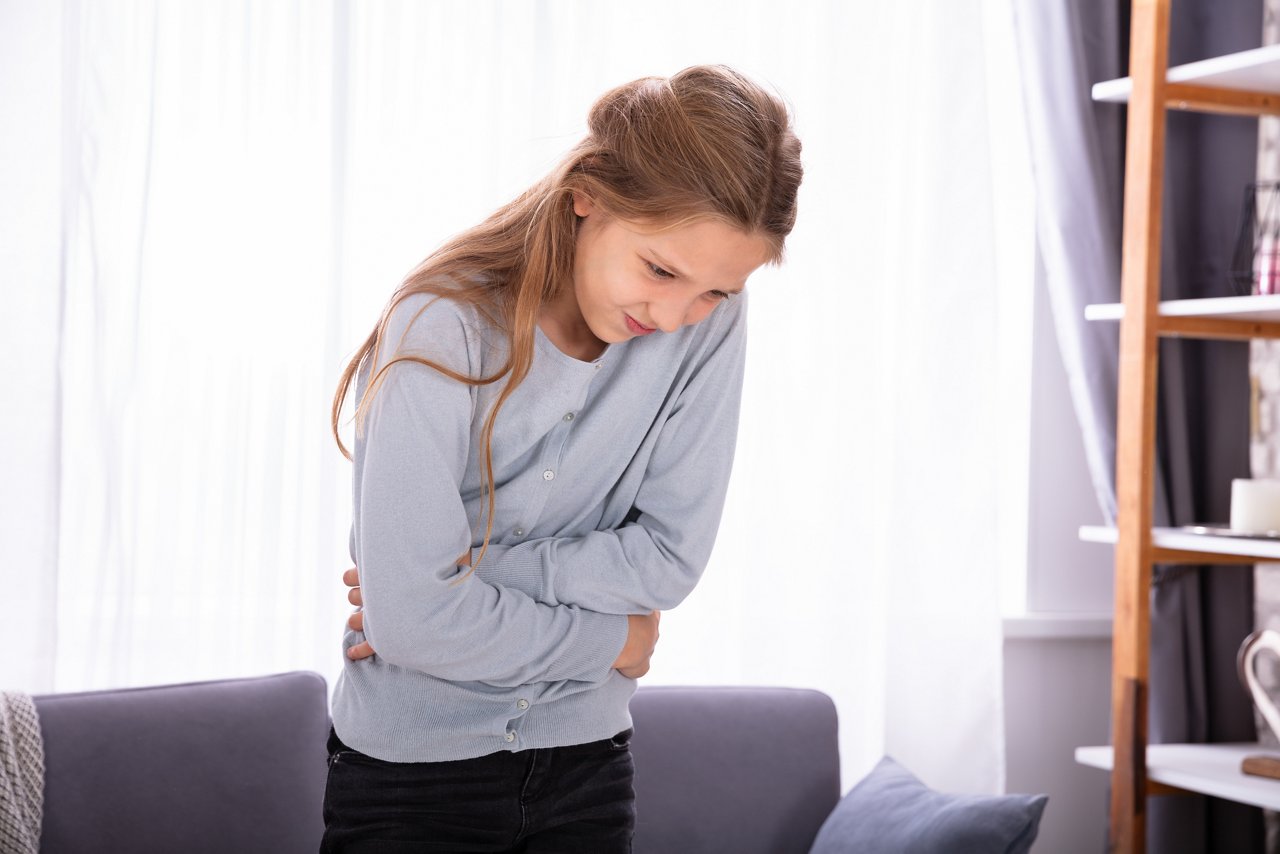 Girl Standing In Front Of Sofa Having Stomach Ache