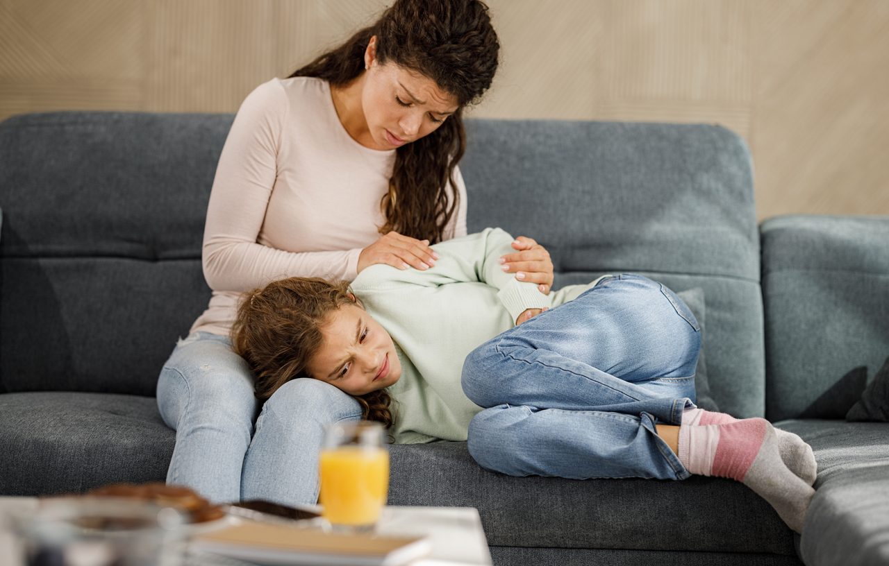 Worried single mother consoling her little girl who is having stomachache at home.